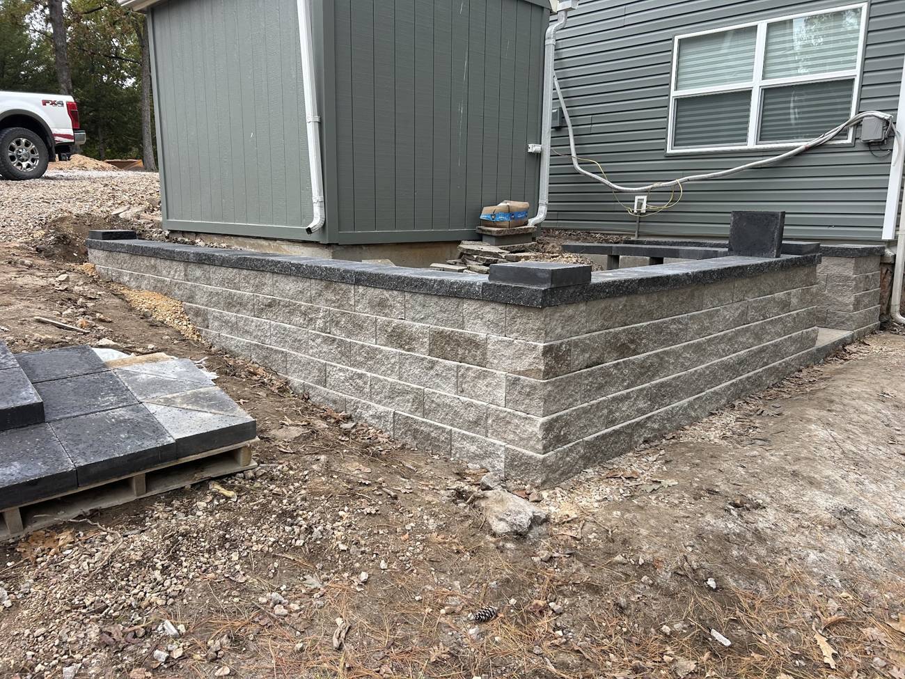 Block retaining wall under construction wrapping the corner of a house