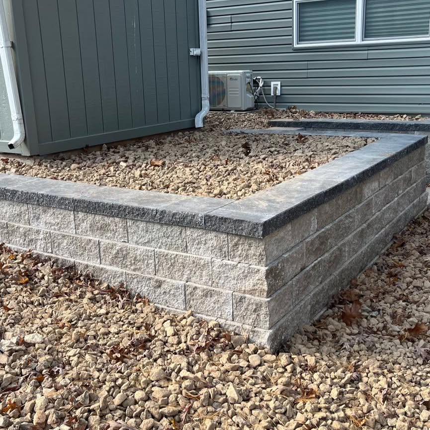 Finished retaining wall corner with dark cap blocks beside a house